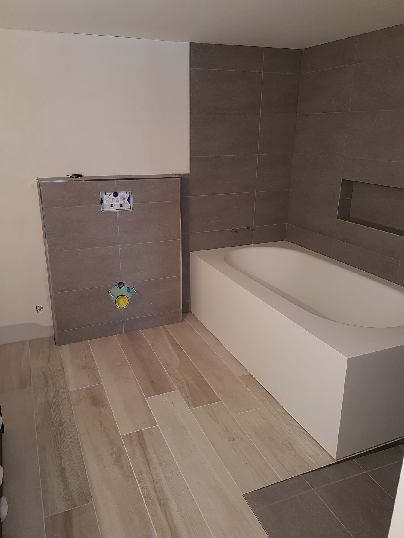 Bad im Umbau mit Wanne, Unterputz-Spülkasten und neuem Bodenbelag in Holzoptik