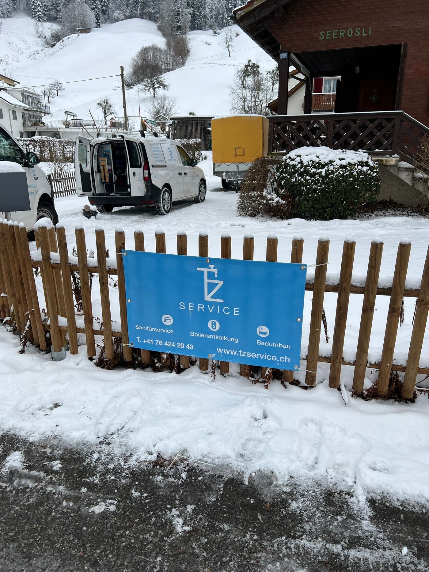 Firmenbanner von TZ Service am Zaun vor dem Hauptsitz, im Hintergrund ein Firmenfahrzeug