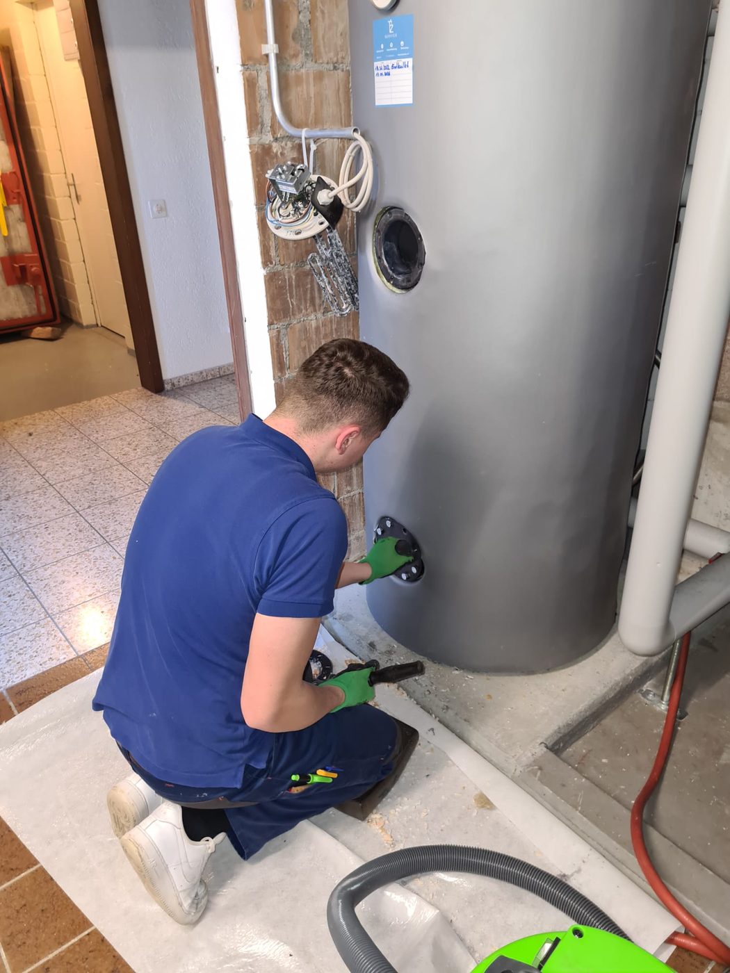 Servicemonteur entkalkt einen Boiler im Keller und saugt Kalk ab