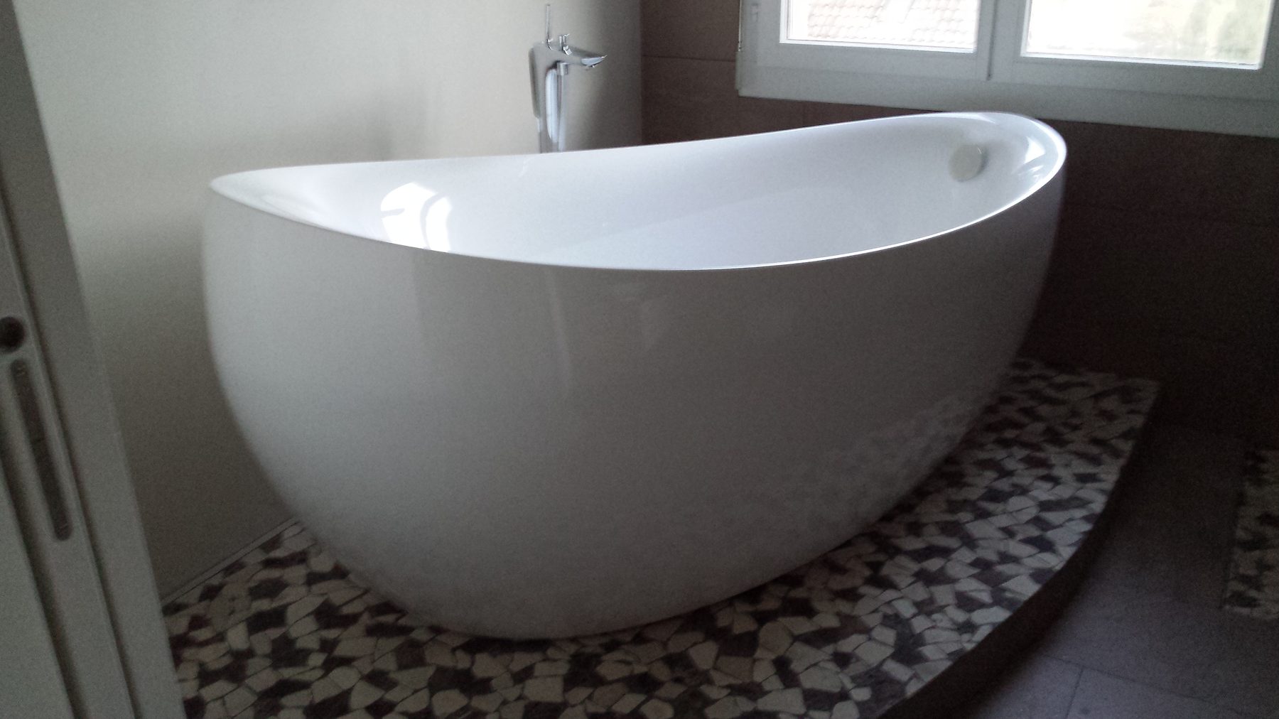 Freistehende, weisse Badewanne auf einem Podest mit Mosaikfliesen