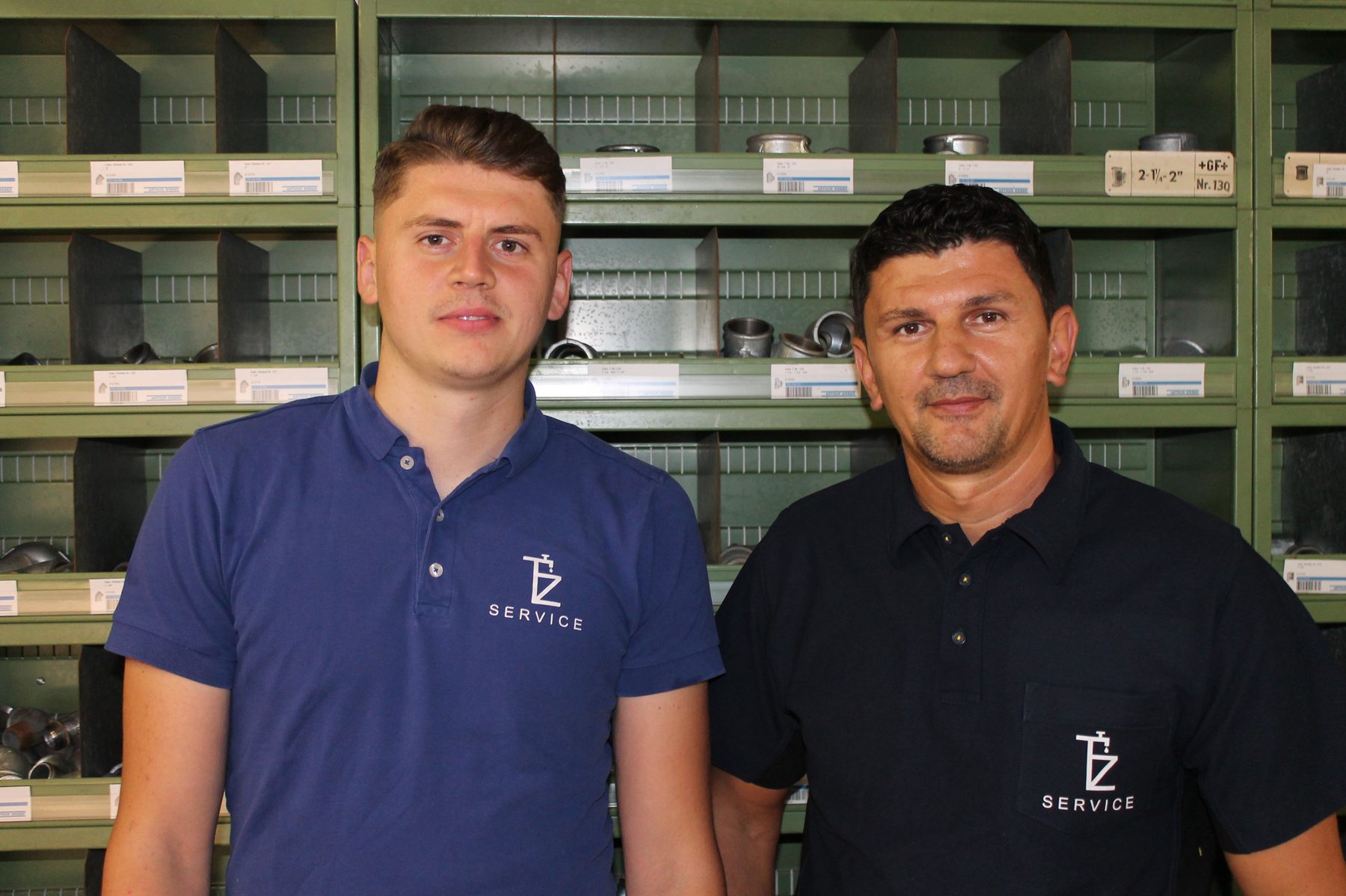 Die beiden Servicemonteure von TZ Service in blauen Poloshirts mit Firmenlogo im Lager